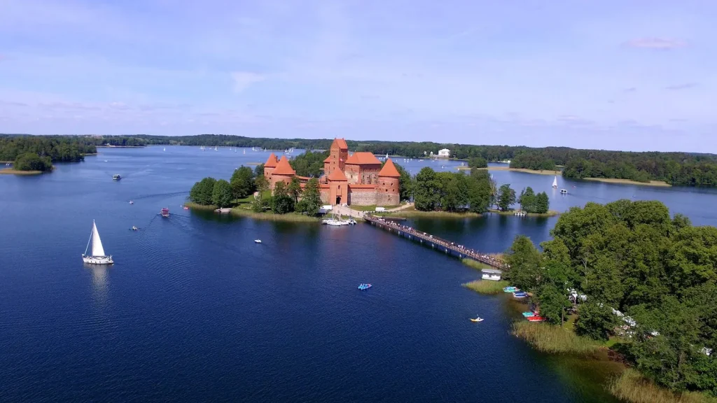 Raudonų plytų pilis ežero saloje ir burlaivis, iš drono